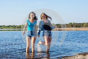 Friends are dancing and splash water on a seashore, laughing. Two women, students are happy on the beach