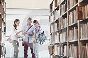 Friends discussing while reading book at library in university