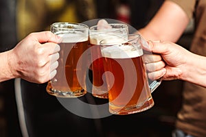 Friends drinking beer at pub. Toast for beer. Men hands raising toast with cold beer mugs at bar