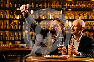 friends drinking beer and taking selfie with smartphone in bar or pub. male friendship - happy.