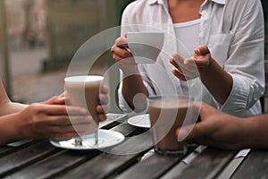 Friends drinking coffee and cocoa at wooden table in outdoor cafe, closeup