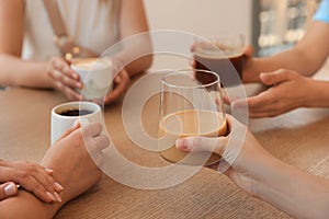 Friends drinking coffee at wooden table in cafe, closeup