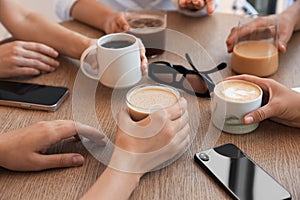 Friends drinking coffee at wooden table in cafe, closeup