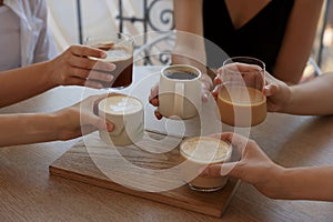 Friends drinking coffee at wooden table in cafe, closeup