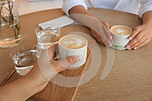 Friends drinking coffee at wooden table in cafe, closeup