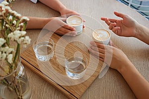 Friends drinking coffee at wooden table in cafe, closeup