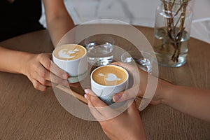 Friends drinking coffee at wooden table in cafe, closeup