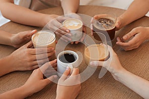 Friends drinking coffee at wooden table in cafe, closeup