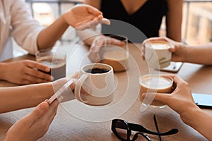 Friends drinking coffee at wooden table in cafe, closeup