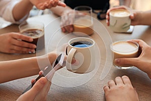 Friends drinking coffee at wooden table in cafe, closeup