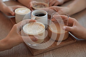Friends drinking coffee at wooden table in cafe, closeup