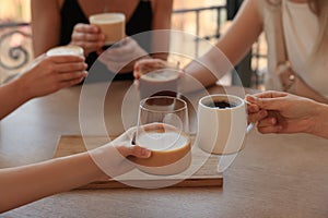 Friends drinking coffee at wooden table in cafe, closeup