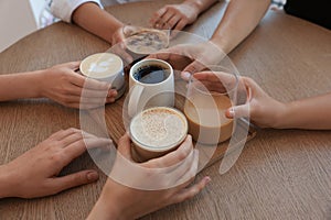 Friends drinking coffee at wooden table in cafe, closeup