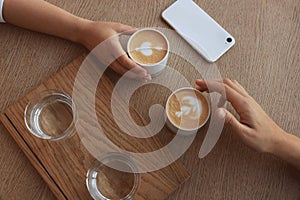 Friends drinking coffee at wooden table in cafe, top view