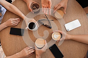 Friends drinking coffee at wooden table in cafe, top view