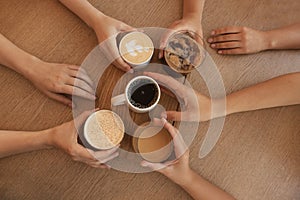 Friends drinking coffee at wooden table in cafe, top view