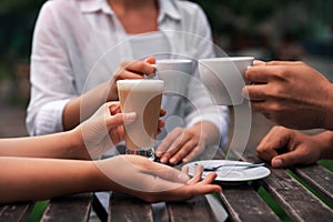 Friends drinking coffee at wooden table in outdoor cafe, closeup