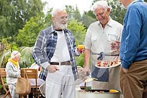 friends with drinks and food standing next to grill during garden party