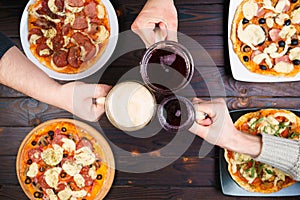 Friends eating pizza. Top view on male hands clinking beer mugs