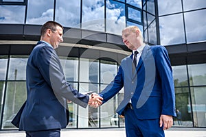 Friends in elegant business suits handshaking outdoors