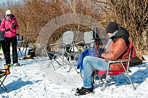 Friends enjoy winter camping with hookah outdoors, camp chairs for smoke and relaxing time together in wild