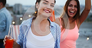 Friends enjoying cocktails at a party. Group of happy people having fun, dancing on a rooftop