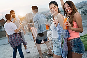 Friends enjoying cocktails at a party. Group of happy people having fun, dancing on a rooftop