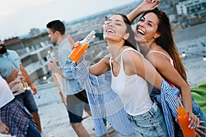 Friends enjoying cocktails at a party. Group of happy people having fun, dancing on a rooftop