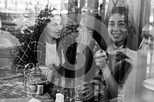 Friends enjoying coffee together in a coffee shop viewed through glass with reflections