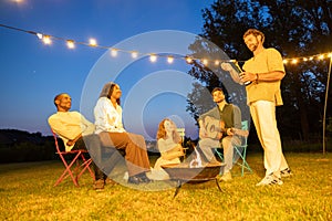 Friends Enjoying a Fireside Guitar Session Under String Lights