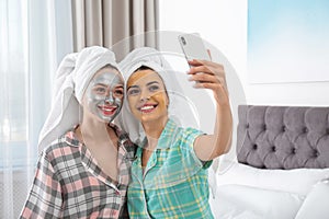 Friends with facial masks taking selfie in bedroom at pamper party