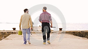 Friends with fishing rods walking along pier