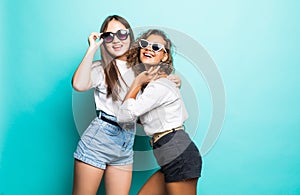 Friends forever. Two mixed race cute lovely girl friends in sunglasses posing with smile on blue background