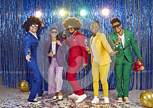 Friends in funny curly wigs and colourful suits in gangnam style on blue background at night club.