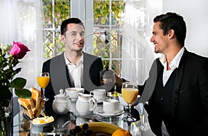 Friends or Gay couple sitting at table in front of patio doors eating breakfast