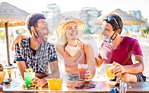 Friends group drinking cocktails at beach with open face masks - New normal vacation concept with people having fun