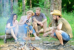 Friends group tourist relaxing near bonfire. Forest hike. Man roasting sausage while friends speak share impression and