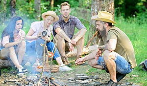 Friends group tourist relaxing near bonfire. Man roasting sausage while friends speak share impression and watching