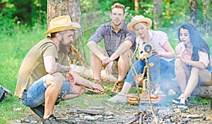 Friends group tourist relaxing near bonfire. Man roasting sausage while friends speak share impression and watching