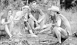 Friends group tourist relaxing near bonfire. Man roasting sausage while friends speak share impression and watching