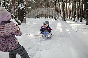 Friends have fun in wonderland, little girl pulls a sledge with brother across winter forest