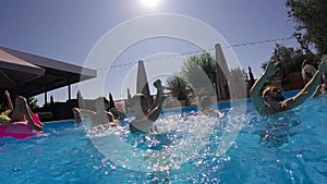 Friends have party in a private villa swimming pool. Happy young people in swimwear splashing water, dancing with