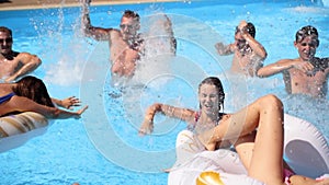 Friends have party in a private villa swimming pool. Happy young people in swimwear splashing water, dancing with