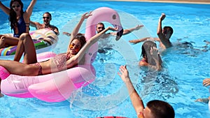 Friends have party in a private villa swimming pool. Happy young people in swimwear splashing water, dancing with