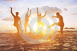 Friends having fun on the beach, silhouettes at sunset in water