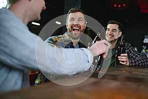 Friends having fun. Happy young men in casual wear drinking beer in pub.