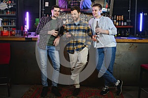 Friends having fun. Happy young men in casual wear drinking beer in pub.