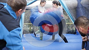 Friends having fun in outdoor amusement park, two men watching women in big boxing gloves boxing on inflatable ring