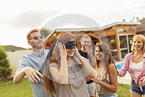 Friends having fun playing blind man`s buff while at poolside summertime outdoor party