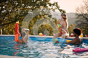 Friends having fun with water guns in pool at summer vacation